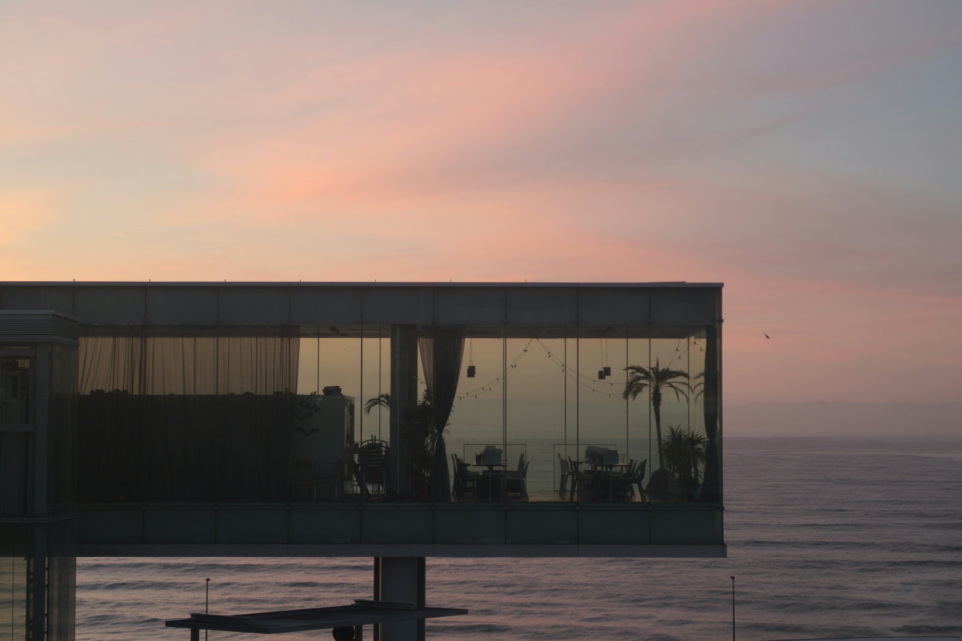 Casa de vidro iluminada diante do mar ao pôr do sol